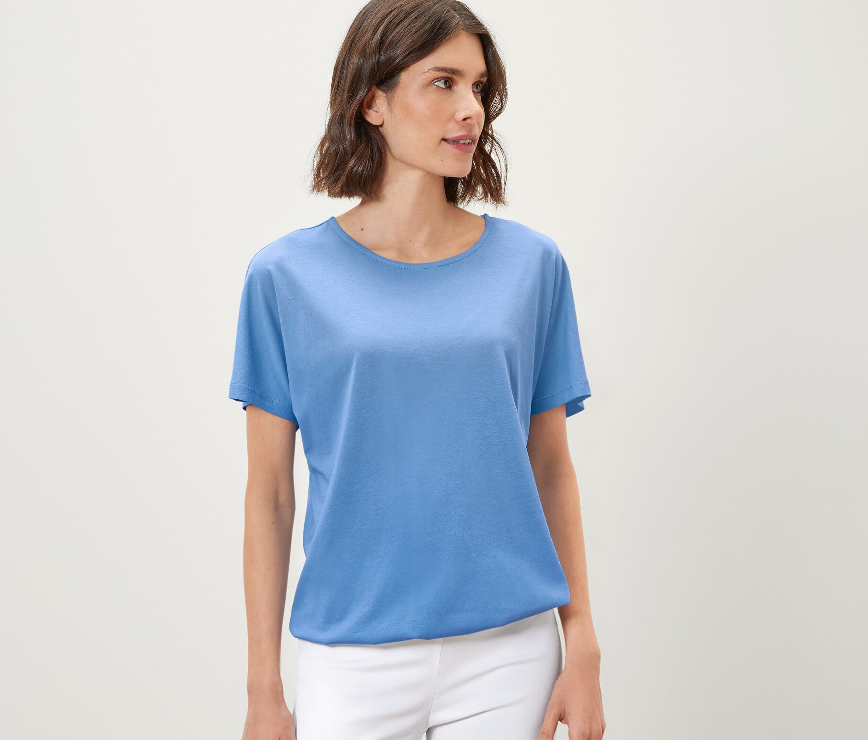 Frau trägt ein hellblaues Blusenshirt und weiße Hosen.
