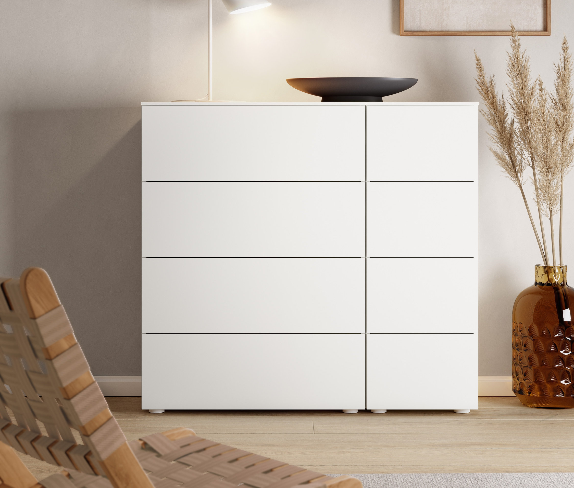 Eine weiße Metall-Tischleuchte »Cale« steht auf einer Kommode mit Schubladen.