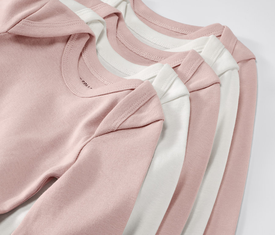 Nahaufnahme von fünf rosa und weißen Baby-Bodys mit Mitwachsfunktion. 5 Baby-Bodys mit Mitwachsfunktion, rosa.