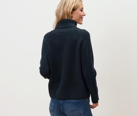 Frau trägt dunkelblauen Grobstrickpullover mit Rollkragen, Jeans und Turnschuhe.