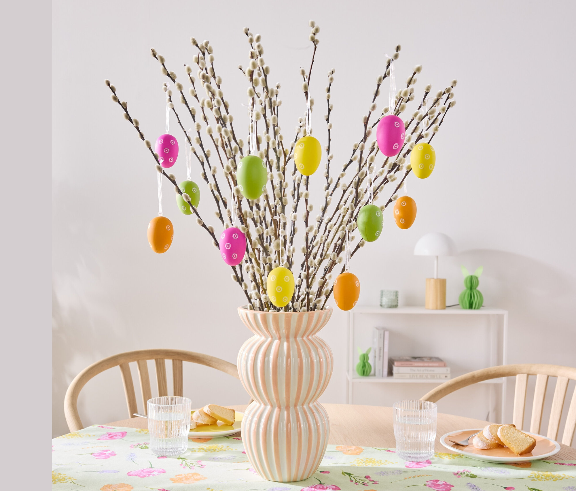 Zweige in einer Vase sind mit 12 Ostereiern, Blumen geschmückt.