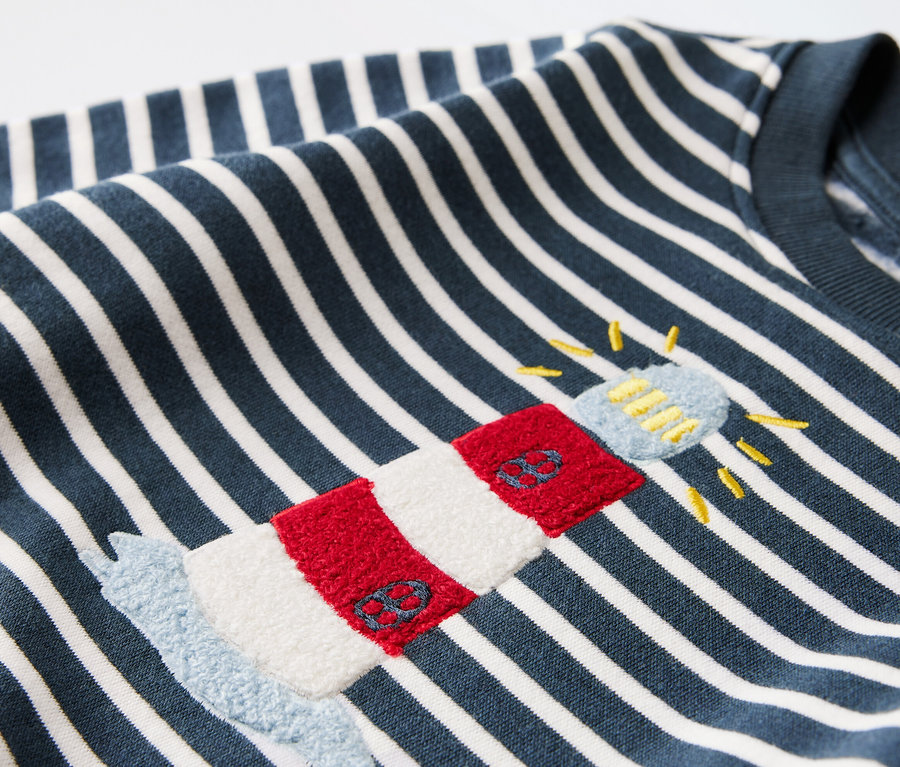 Detailaufnahme eines Baby-Sweatshirts mit blau-weißem Streifenmuster und Leuchtturm-Applikation.