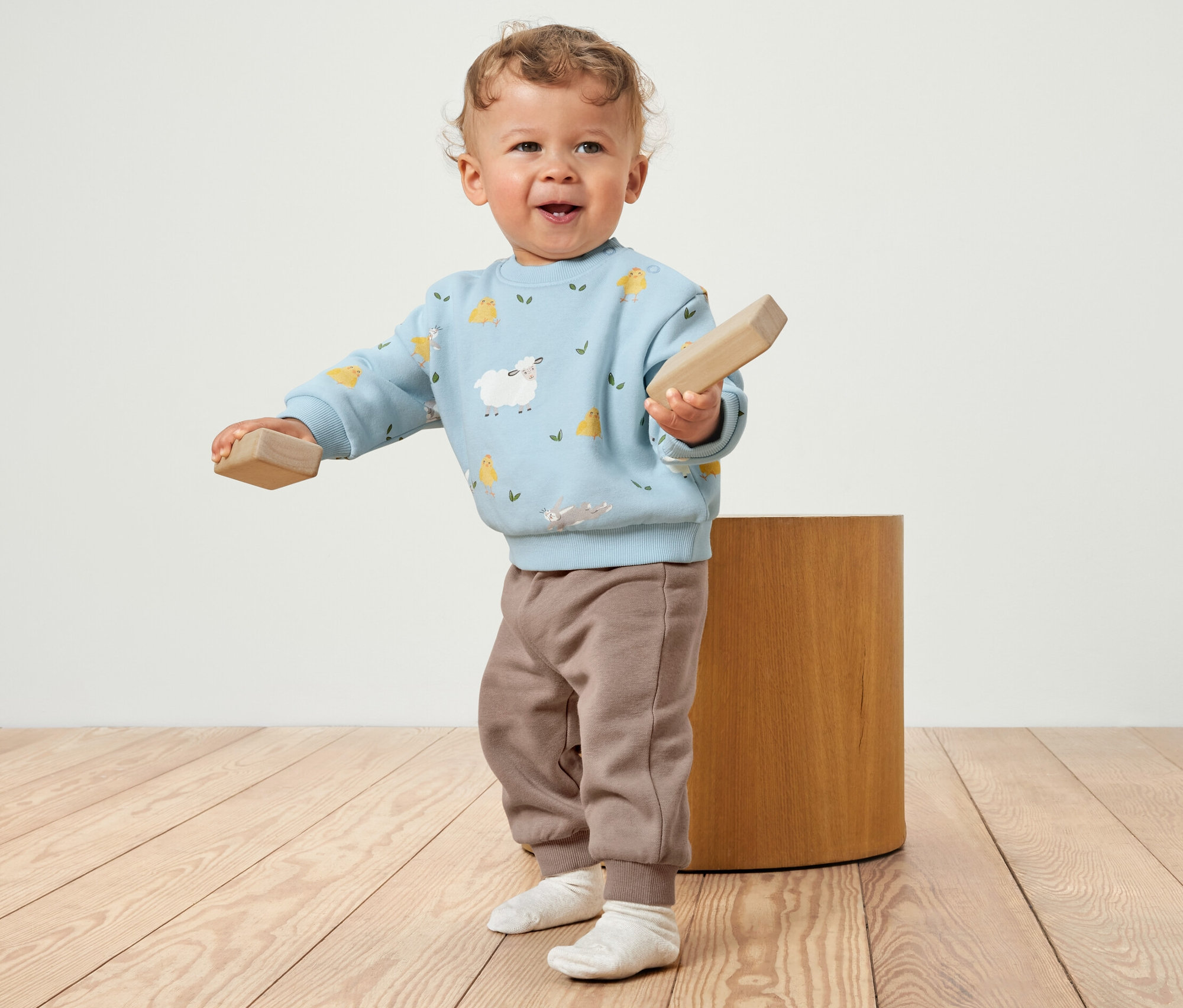 Kleinkind hält Holzklötze, bekleidet mit einem Baby-Sweat-Set mit angerauter Innenseite.