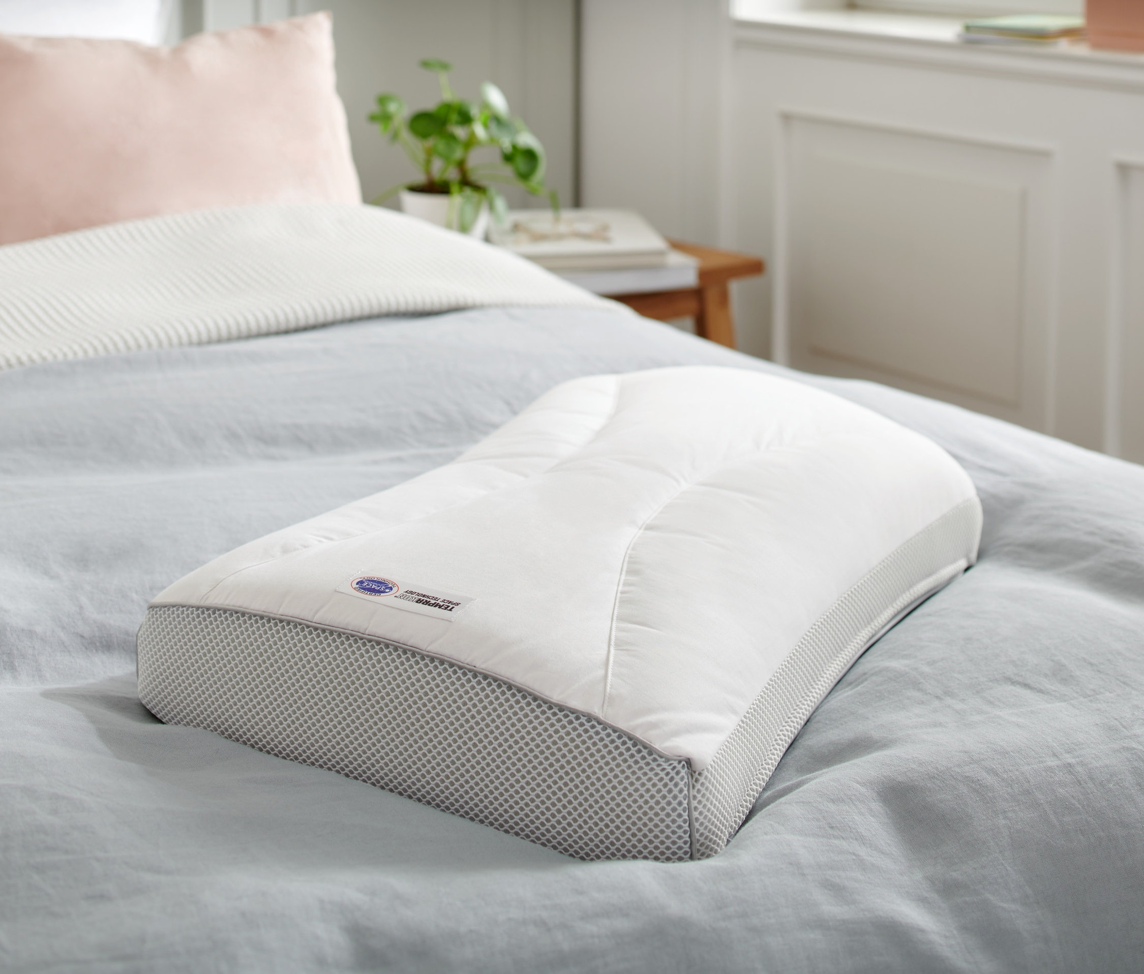 Ein Temprakon X-Zone Kissen liegt auf einem Bett mit blauem Überwurf.