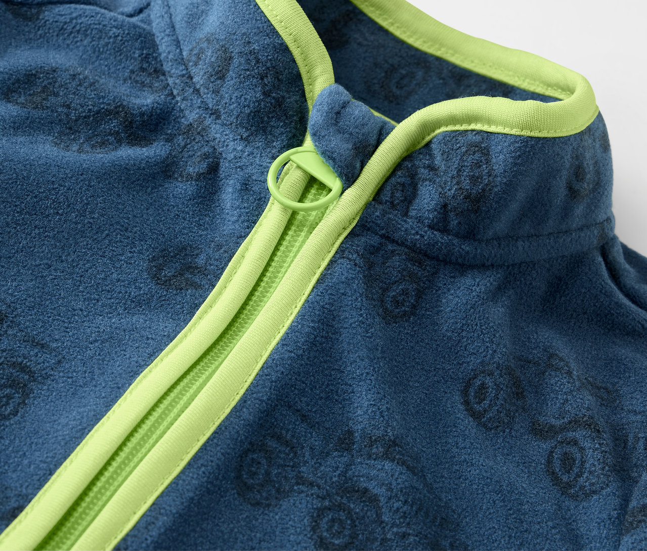 Detailansicht einer blauen Kinder-Fleecejacke mit Truck-Muster und hellgrünem Reißverschluss.
