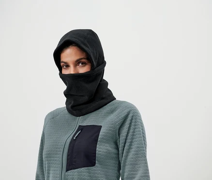 Frau mit braunen Augen trägt eine schwarze Sturmhaube und eine Sweatshirtjacke mit Reissverschluss und Tasche.