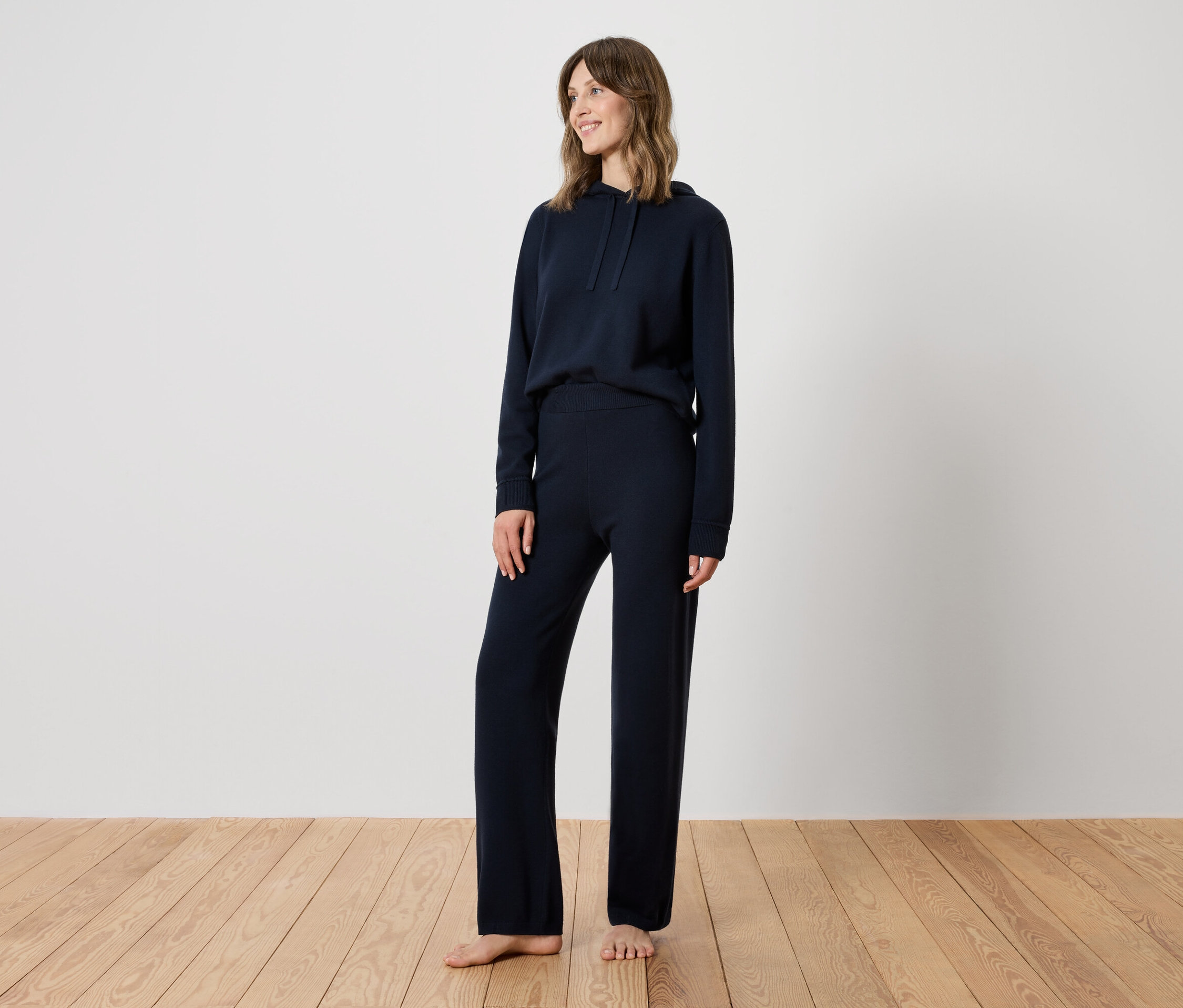 Eine Frau steht auf einem Holzboden und trägt einen dunkelblauen Trainingsanzug.