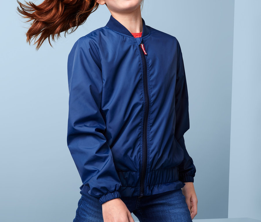 Ein Mädchen mit einem roten Pferdeschwanz posiert in einer recycelten Bomberjacke und Jeans.