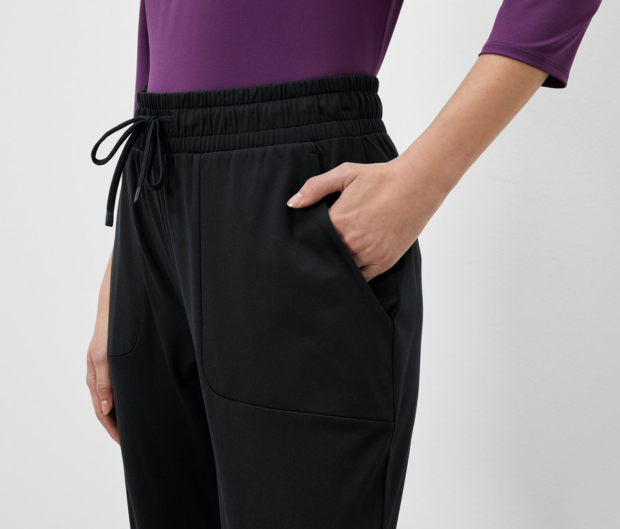 Teilansicht einer Person in schwarzer Trainingshose mit einer Hand in der Hosentasche.