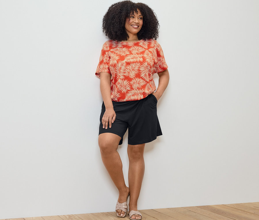 Frau posiert in bedrucktem Blusenshirt und schwarzen Jerseyshorts.