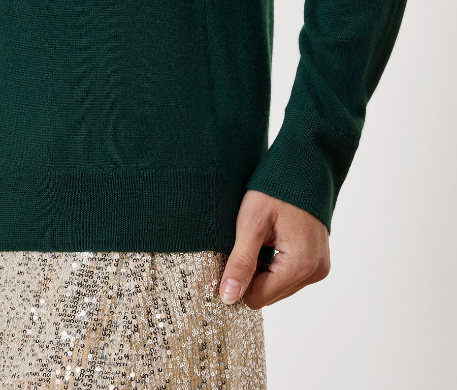 Detail eines Damenoutfits: grüner Pullover und goldener Paillettenrock.