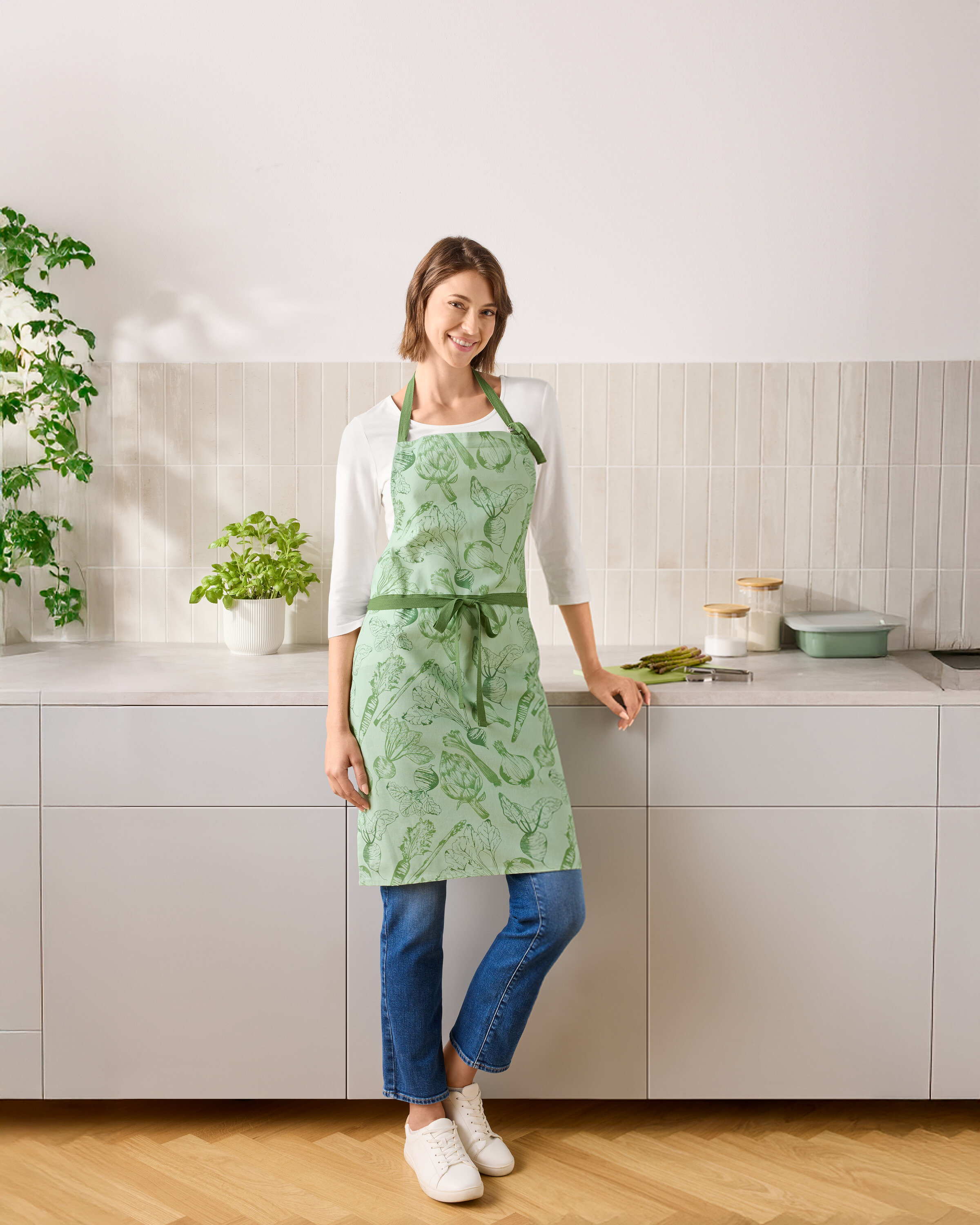 Eine Frau steht in einer Küche und trägt eine grüne Gemüseschürze.