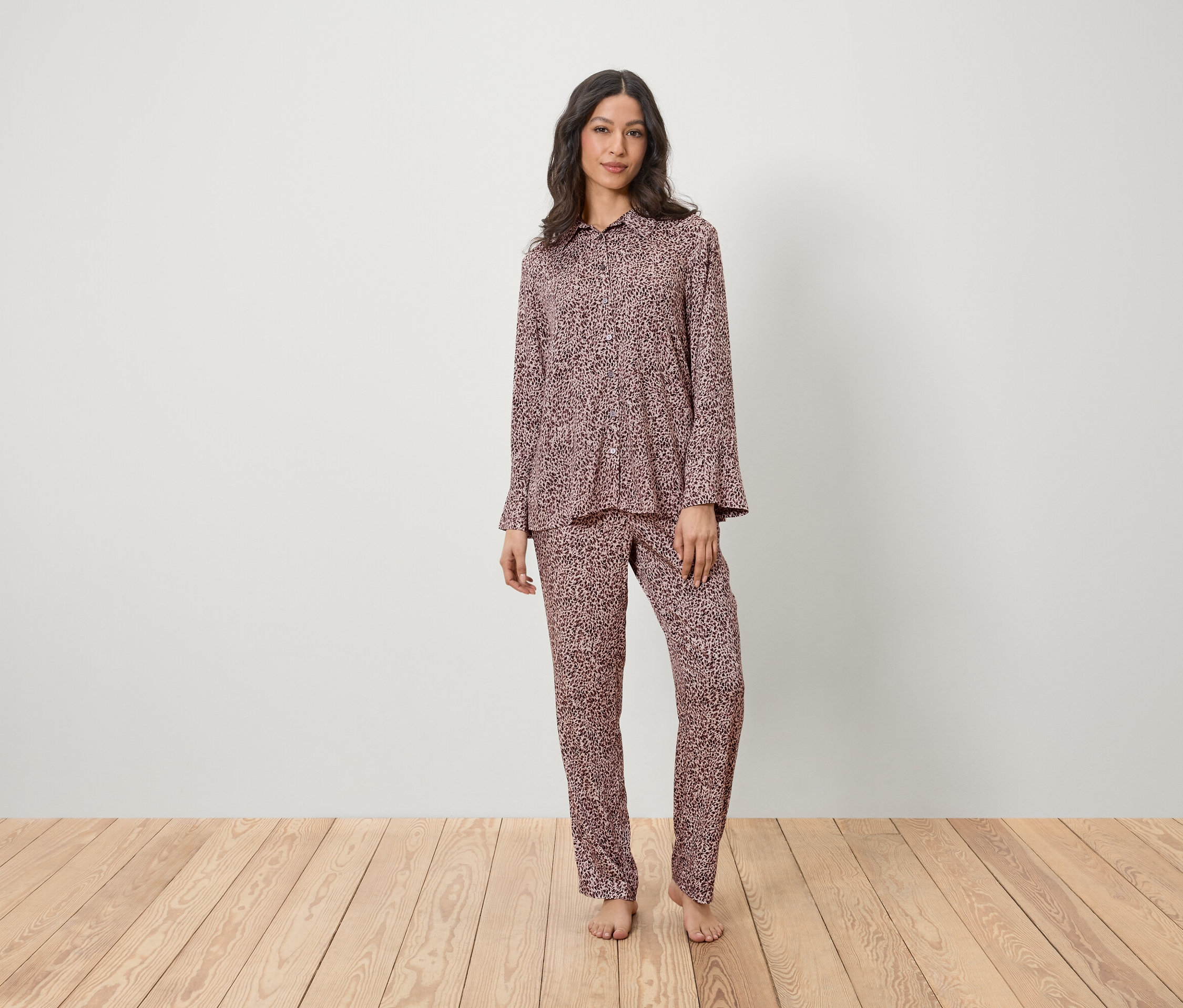 Eine Frau steht auf einem Holzboden und trägt einen rosafarbenen Pyjama mit Muster.