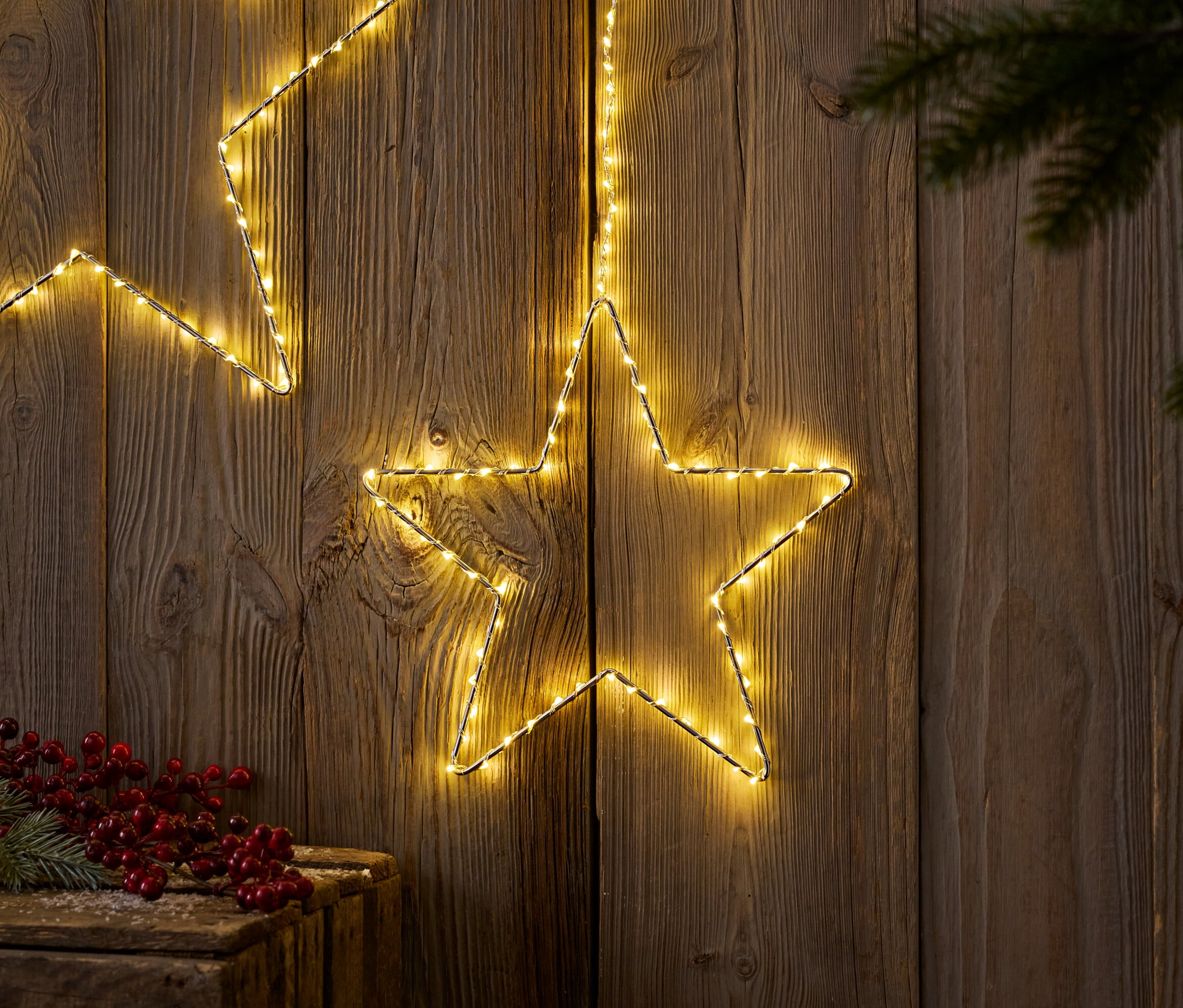 Zwei leuchtende Sterne vor Holz mit Tannenzweig und roten Beeren.