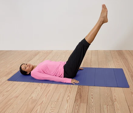 Frau liegt auf einer blauen Yogamatte, die Beine angehoben.