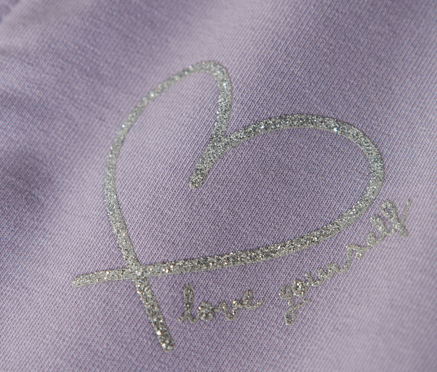 Nahaufnahme eines lila Kleidungsstücks mit einem glitzernden Herzdesign und dem Text "love yourself".