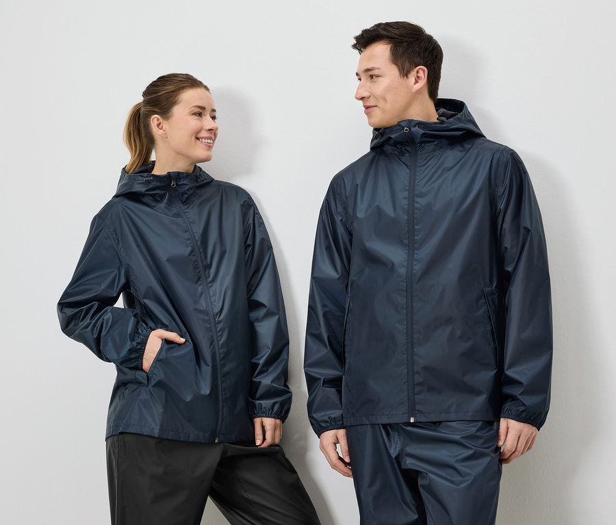 Eine Frau mit Pferdeschwanz und ein Mann tragen marineblaue Regenjacken und Regenhosen vor einem weißen Hintergrund.