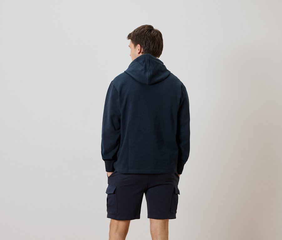 Mann von hinten in marineblauem Kapuzenpullover und Shorts.