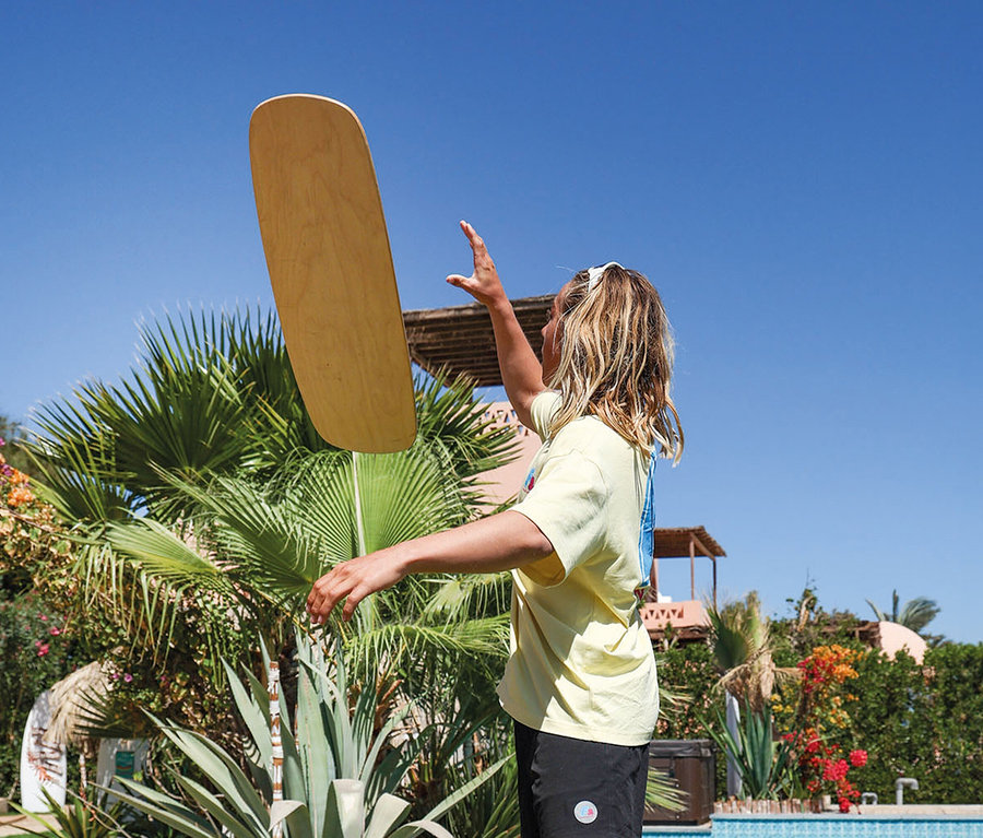 Junge balanciert ein F2 Cork Balance Board Set Pill mit Korkrolle in der Luft, im Hintergrund Palmen und ein Pool.