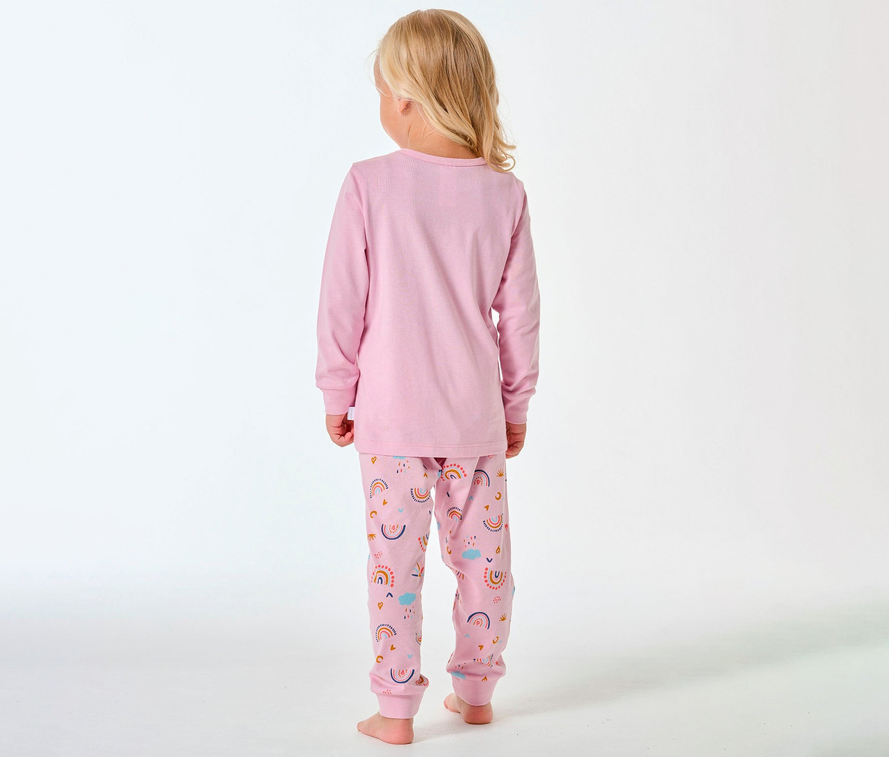Kind von hinten, mit blonden Haaren, trägt einen langen Kinder-Pyjama von SCHIESSER mit Regenbogenmuster.