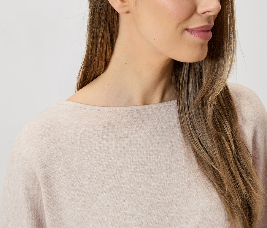 Nahaufnahme einer Frau mit langen braunen Haaren, die einen hellrosa Pullover mit Rundhalsausschnitt trägt.
