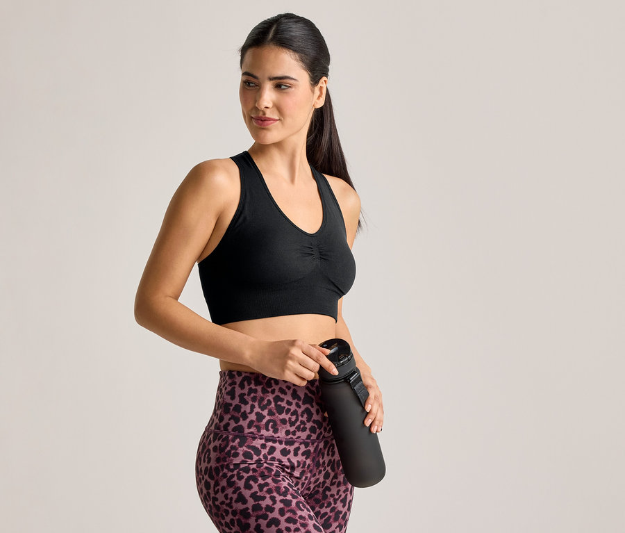 Frau im Sport-BH und Leggings mit Leopardenmuster hält eine schwarze Wasserflasche.