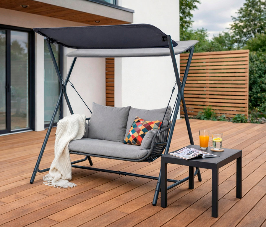 Leco Hollywoodschaukel mit Kissen und Decke auf einer Holzterrasse, neben einem Tisch mit Getränken und einer Zeitschrift.