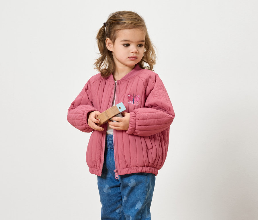 Mädchen mit rosafarbener Jacke hält Holzspielzeug in den Händen.
