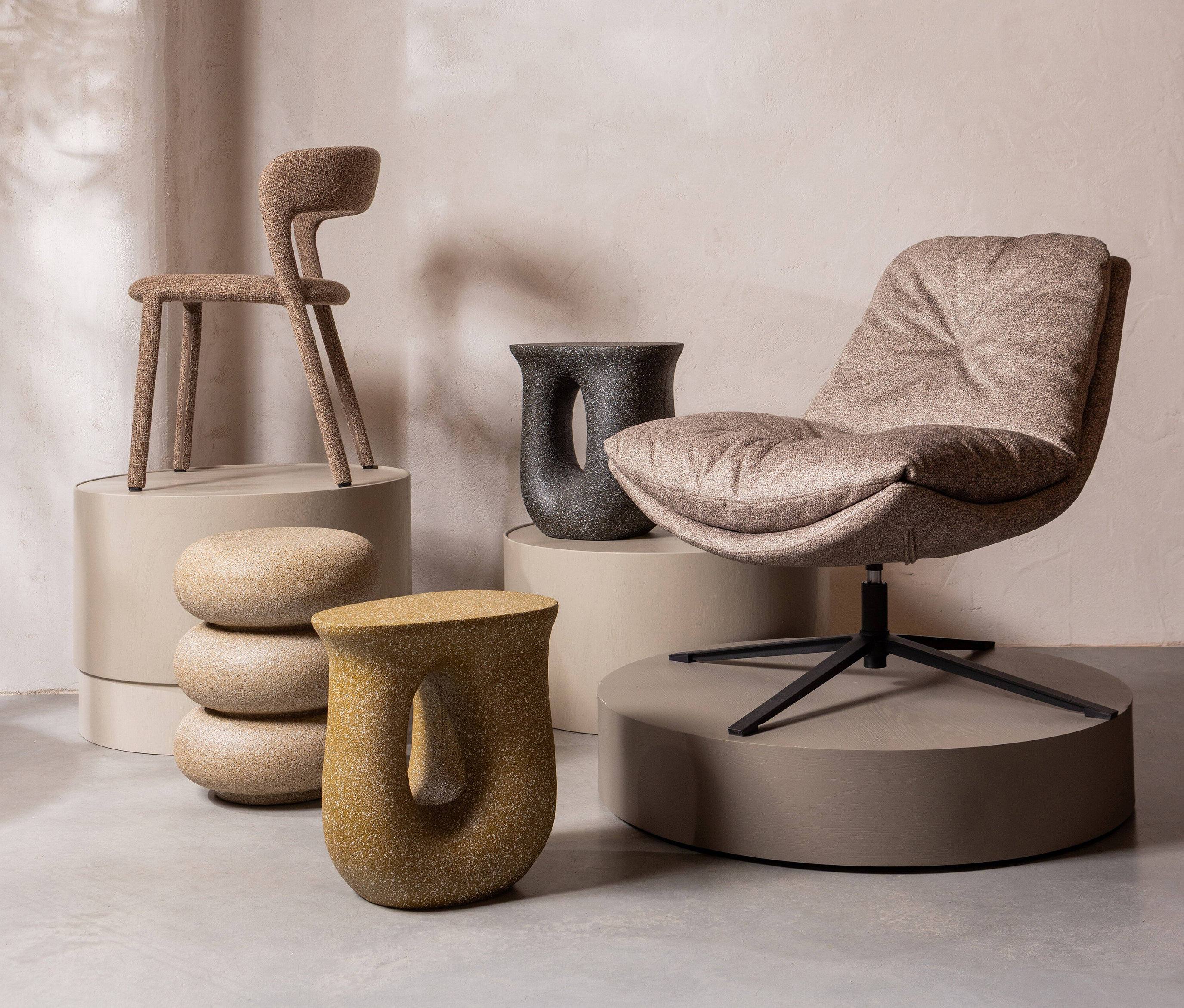 Möbelszene mit einem Stuhl auf einem Sockel, einem Sessel, einem schwarzen Tisch und dekorativen Steinhockern.