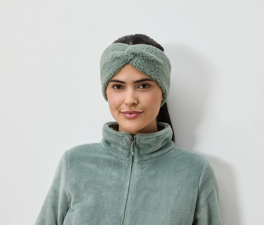 Frau mit olivgrünem Stirnband und Fleecejacke vor weißem Hintergrund.