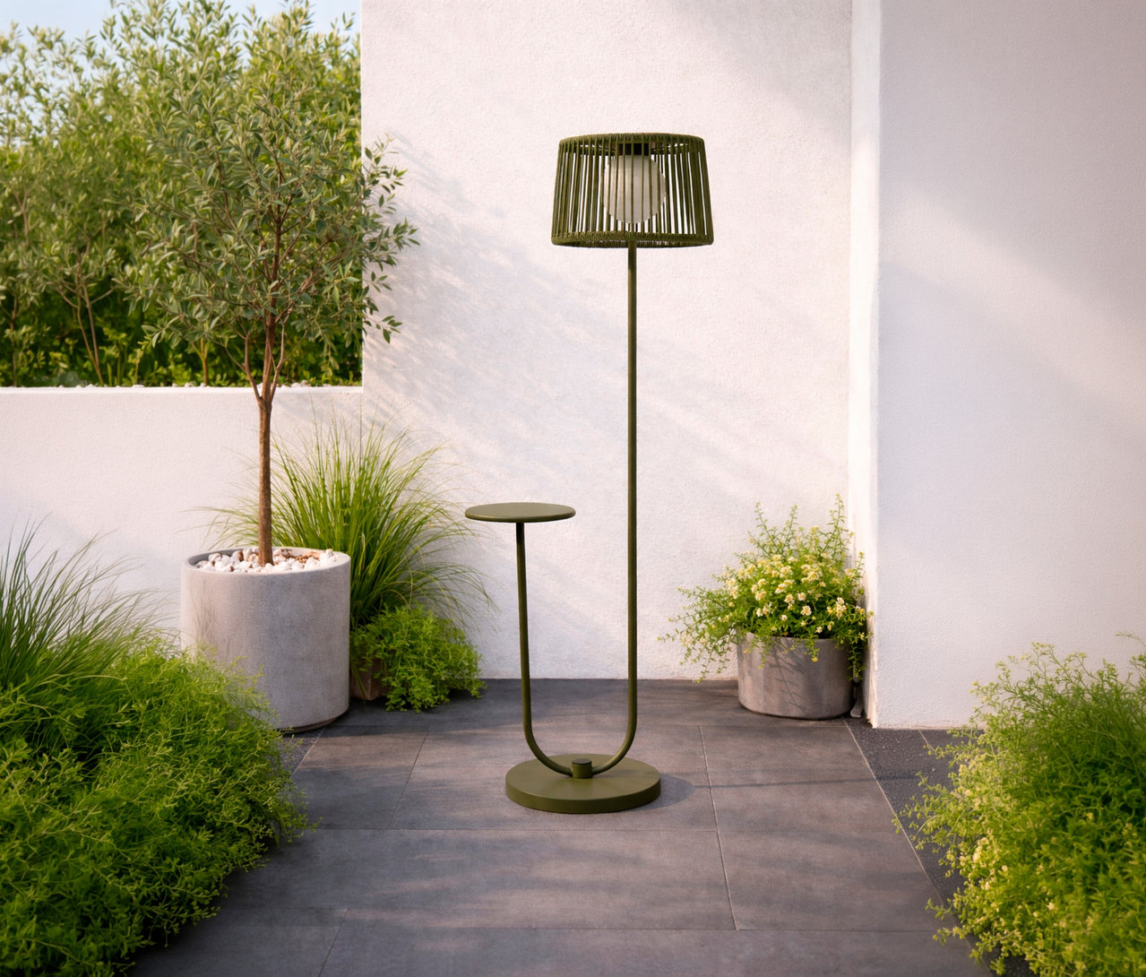 Grüne Leco Solar Stehleuchte mit integriertem Tisch auf einer Terrasse neben einem Baum und Pflanzen.