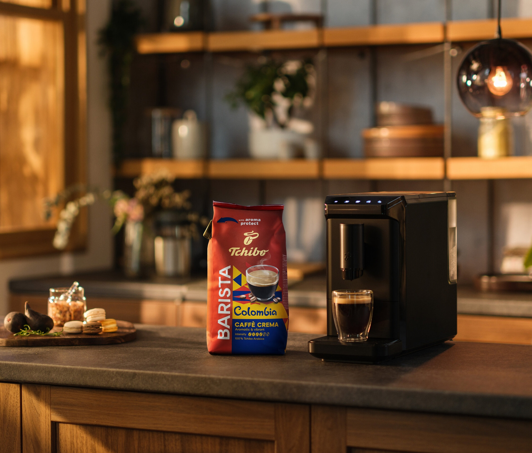 Auf einer Küchentheke stehen eine Kaffeemaschine, eine Tasse Kaffee und eine Packung BARISTA Origins Colombia - 1 kg Ganze Bohne.