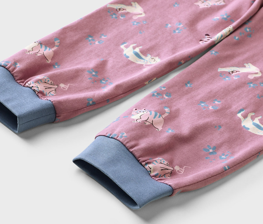 Zwei rosa Kleidungsärmel mit blauen Rippbündchen, die ein Muster aus weißen und blauen Katzen und kleinen blauen Blumen aufweisen.