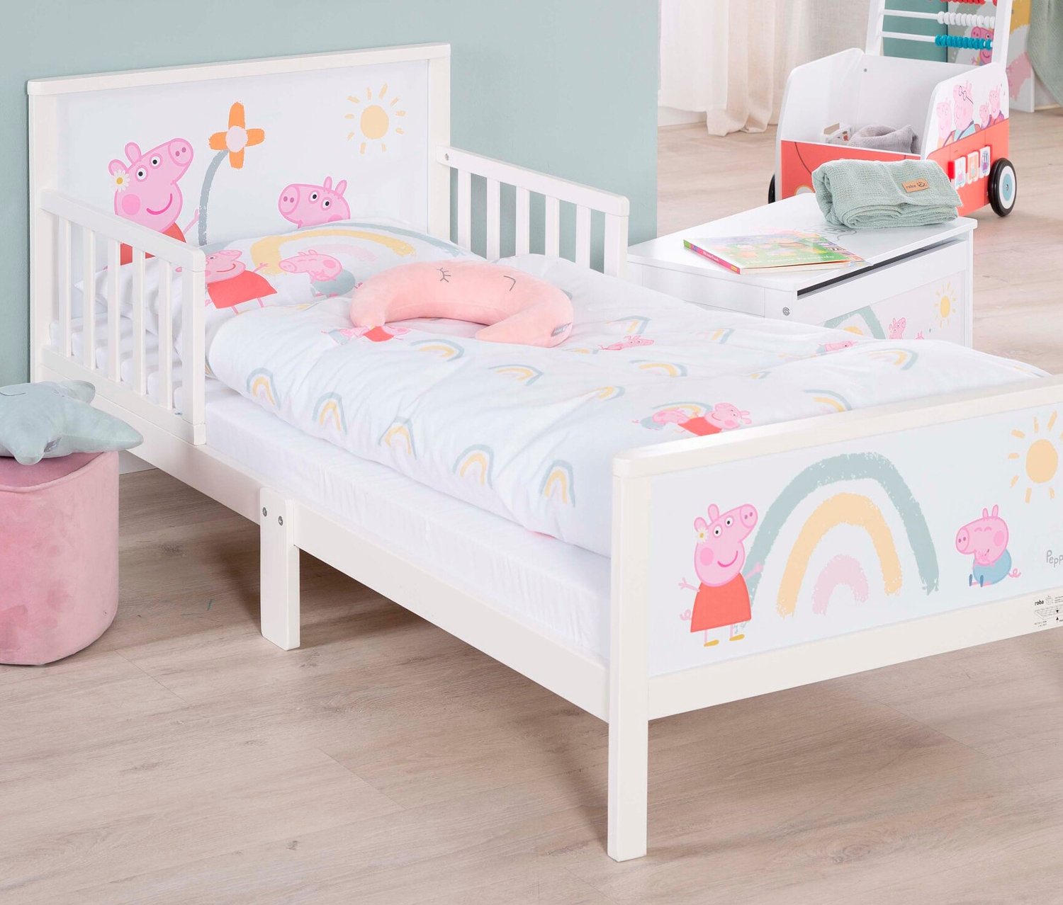Weißes Kinderbett mit Peppa Pig-Motiv, rosa Kissen und Spielzeugkiste im Hintergrund.