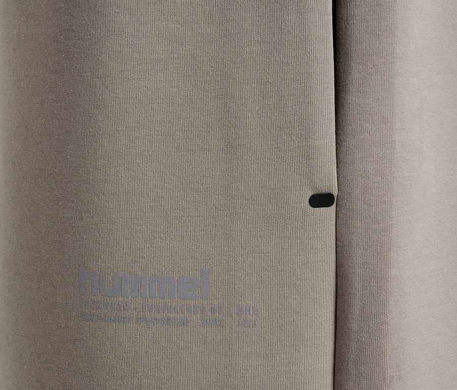 Nahaufnahme von grauer Sportbekleidung mit kleinem, dunklem Knopf und reflektierendem "hummel"-Logo.