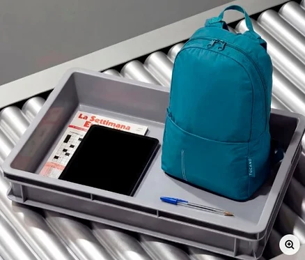 Blauer Tucano Rucksack »Compatto Eco«, Tablet, Zeitschrift und Stift in einer grauen Sicherheitsschale auf einem Rollband.