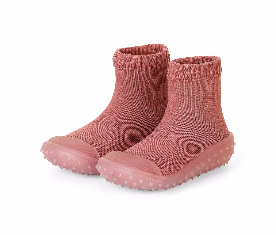 Ein Paar rosafarbene Babysocken-Schuhe mit geripptem Schaft und transparenter, genoppter Sohle.