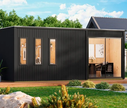 Ein modernes schwarzes Modulgebäude mit vertikaler Verkleidung und einer Holzterrasse steht in einem grünen Garten. Drei schmale Fenster links zeigen Regale mit Dekoration, während eine große Glasschiebetür rechts einen Essbereich mit Tisch, Stühlen, Blumen und Kunst offenbart.
