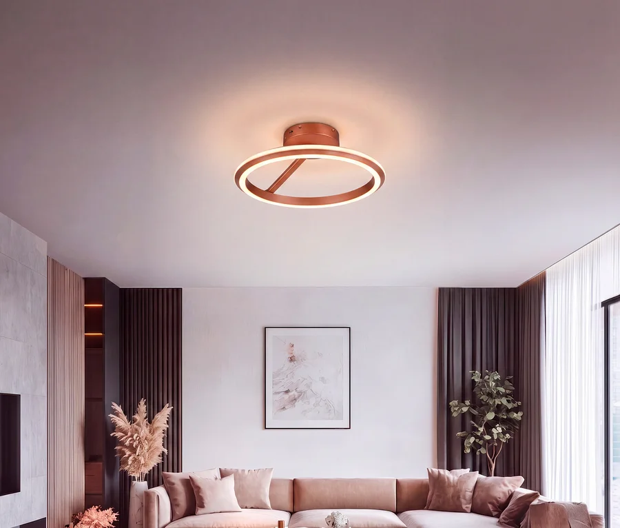 Modernes Wohnzimmer mit einer roségoldenen runden Deckenleuchte, die ein beiges Ecksofa, abstrakte Kunst, Pampasgras und eine Topfpflanze beleuchtet.