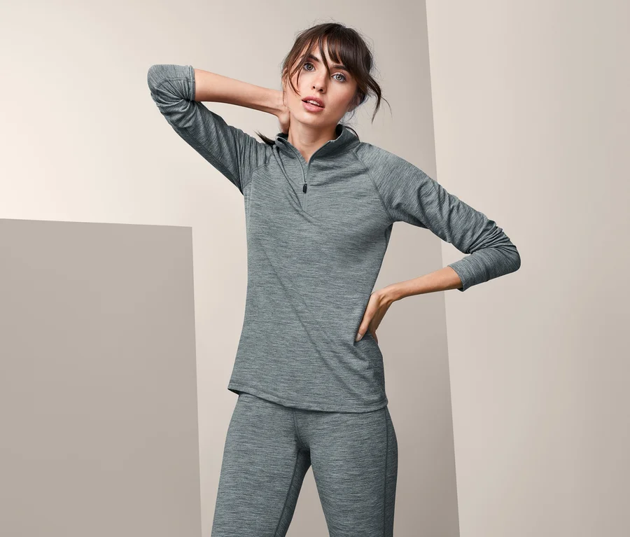 Frau posiert in grauem Funktionsshirt mit Merinowolle und Hose.
