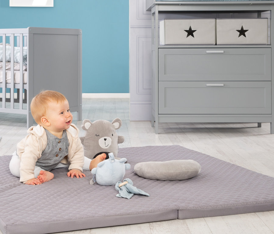Baby sitzt auf roba Spiel- und Krabbelmatratze mit Spielzeug.