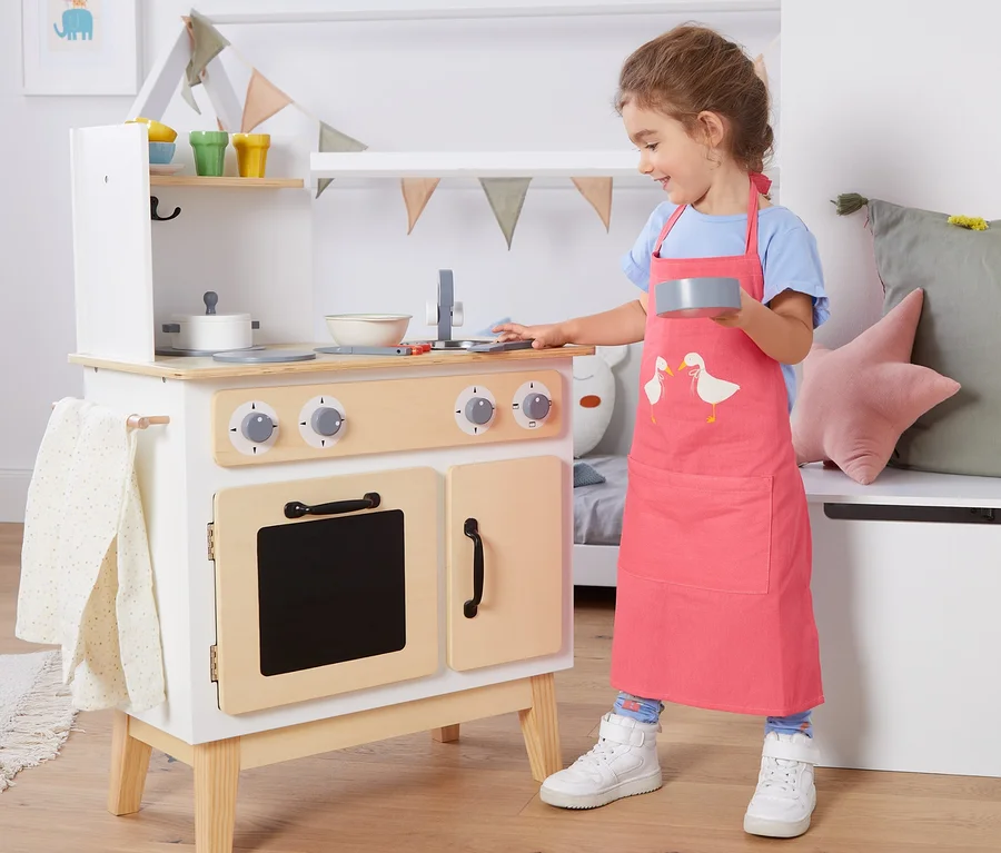 Mädchen spielt mit Spielküche und trägt eine Kinder-Küchenschürze.