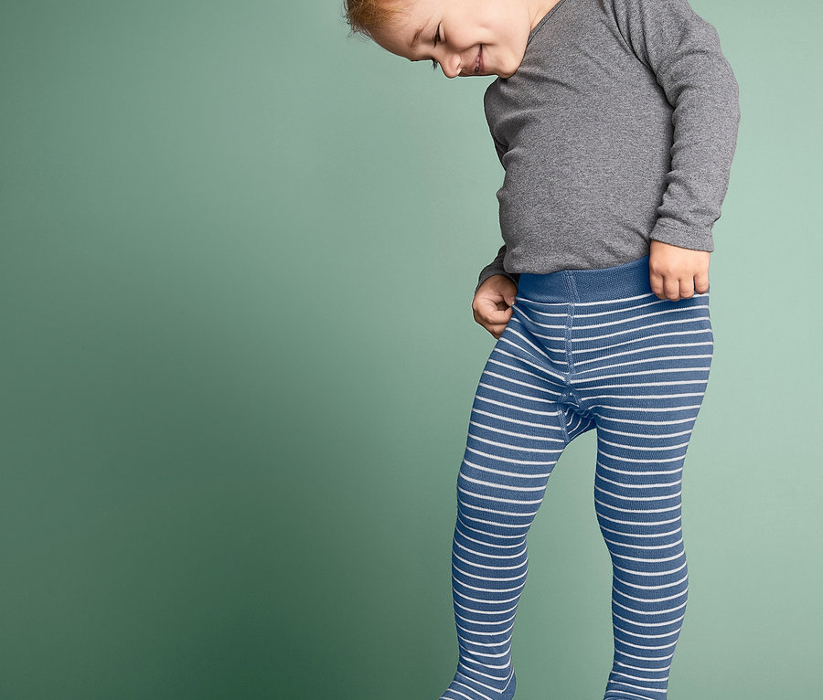 Ein Junge mit blonden Haaren trägt ein graues Oberteil und eine blau-weiß gestreifte Strumpfhose (3 Stück).
