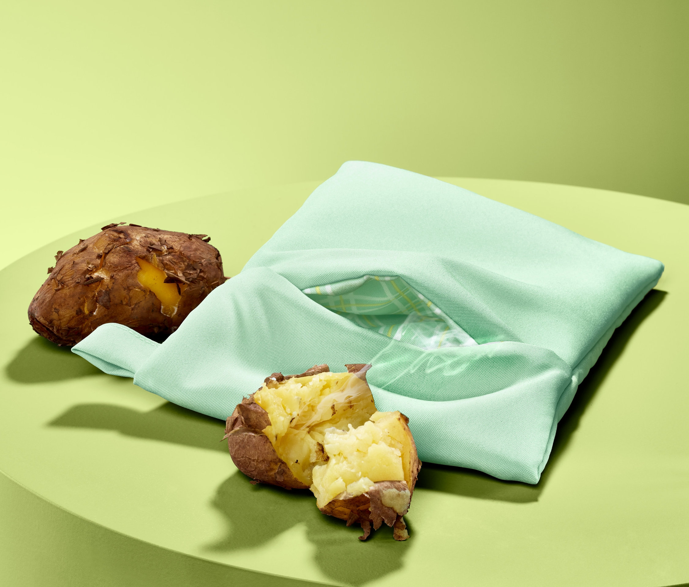 Gekochte Kartoffeln und eine Mikrowellen-Kartoffelgartasche auf einem grünen Tisch.