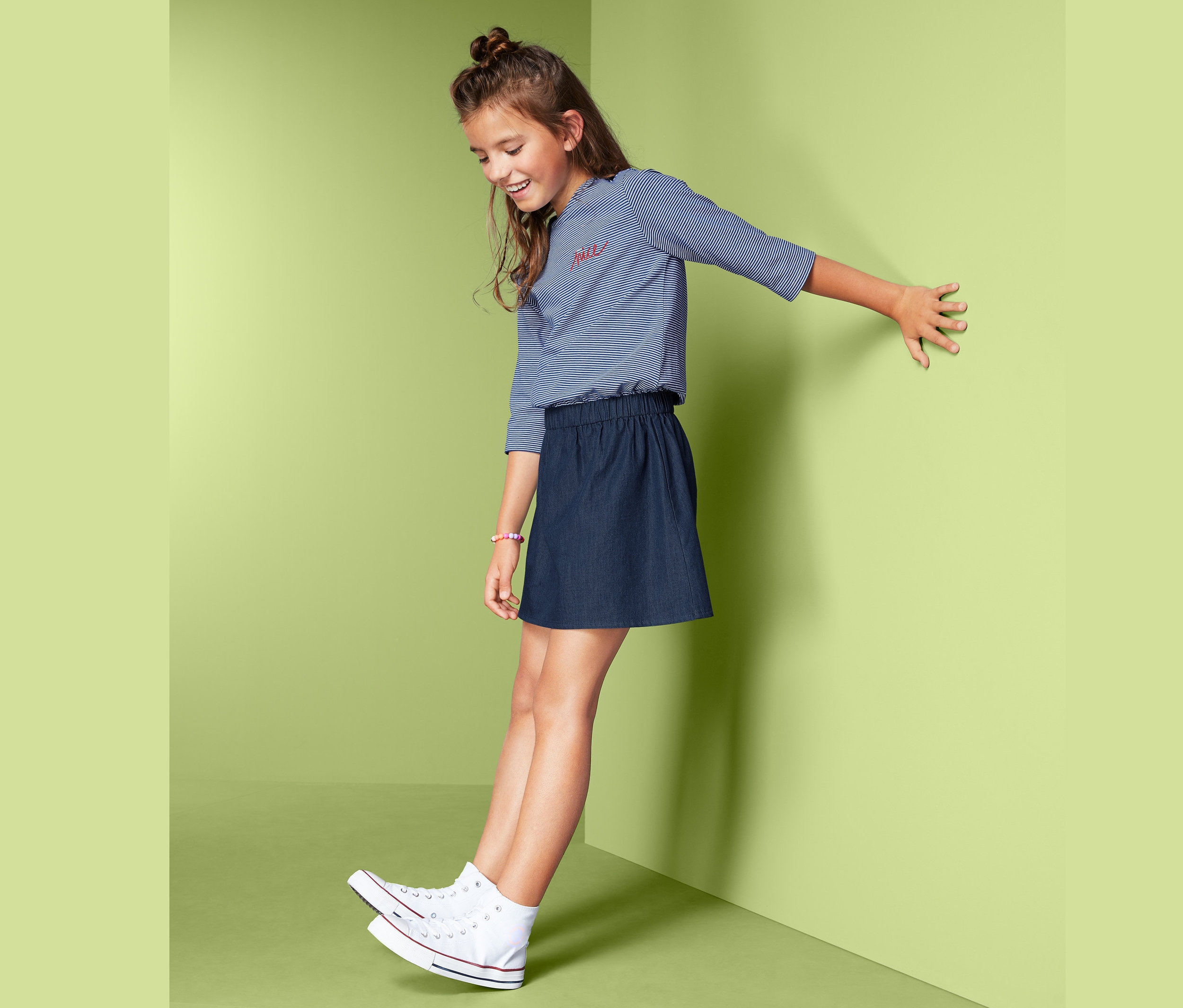 Mädchen posiert im Kleid im Materialmix an einer Wand.