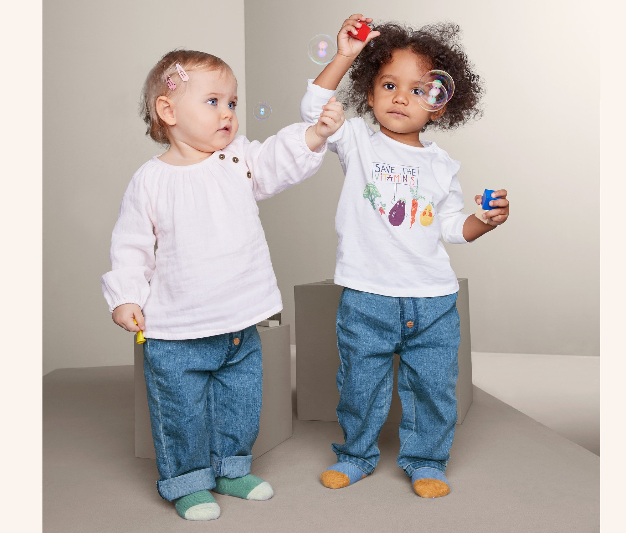 Zwei Kinder machen Seifenblasen und tragen Schlupfhosen in Jeansoptik.