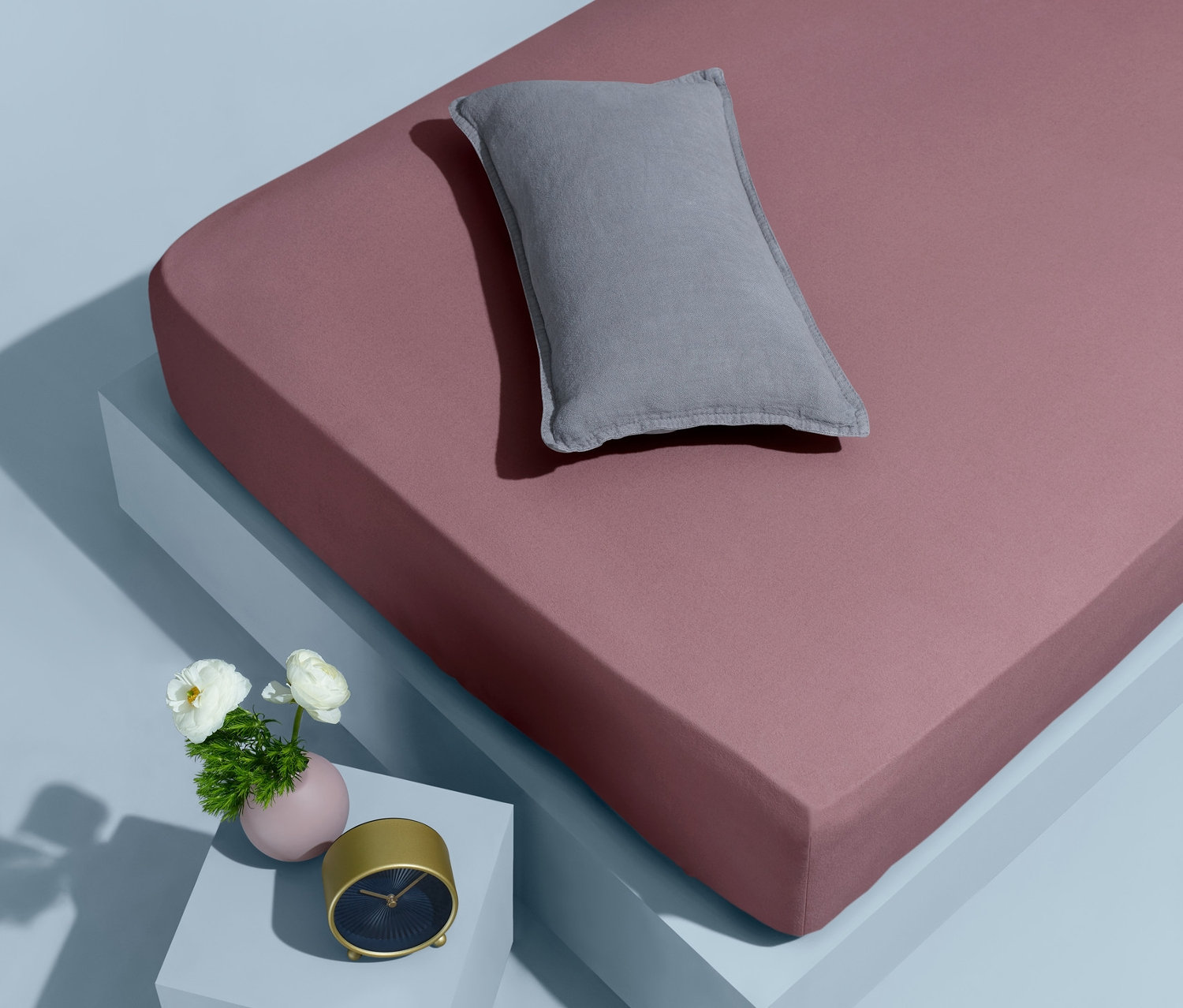 Rosa Biber-Spannbettlaken in Normalgröße mit grauem Kissen, Wecker und Blumen.