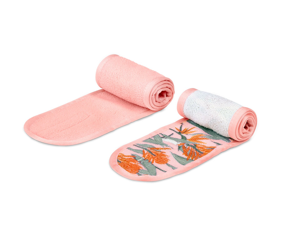 Zwei Kosmetik-Stirnbänder, eines rosa und eines mit tropischem Muster, liegen nebeneinander.