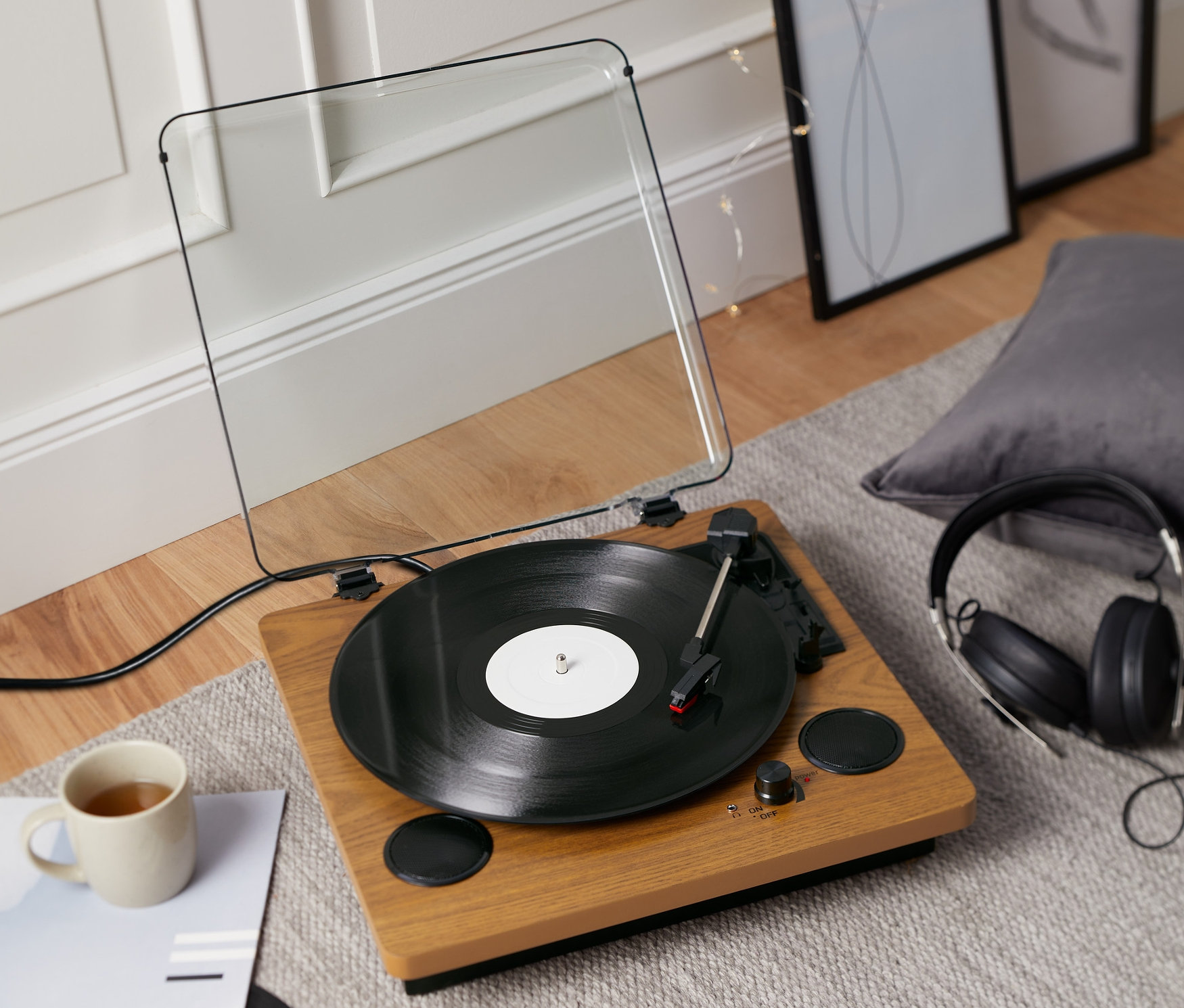 Ein »Dual DTR 61« Schallplattenspieler mit integrierten Lautsprechern spielt eine Schallplatte ab. Daneben stehen eine Tasse und Kopfhörer.