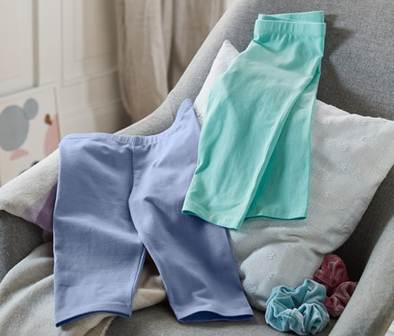 Türkise und mittelblaue 3/4-Leggings liegen auf einem grauen Stuhl.